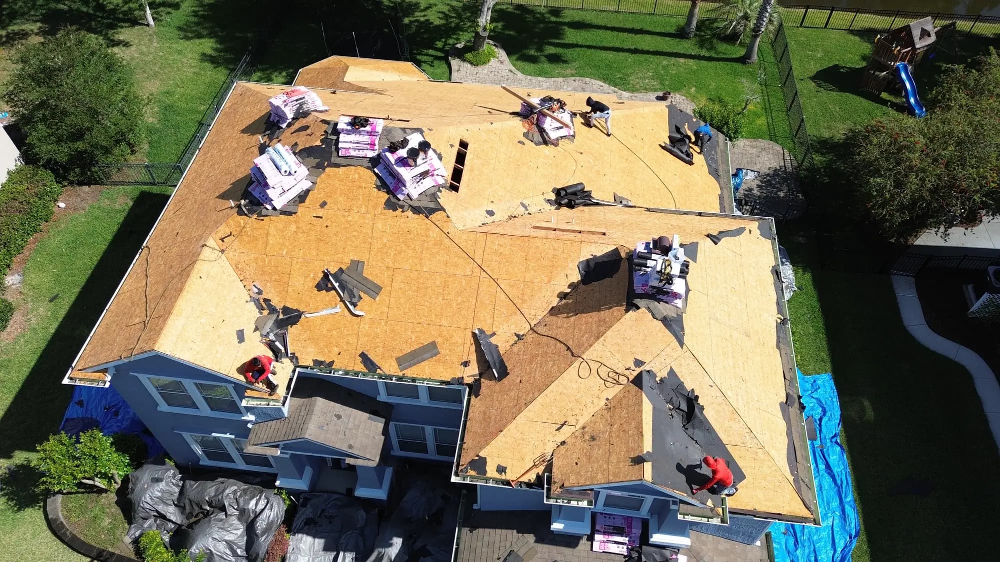 Owens Corning shingle bundles staged across exposed roof decking with crew members working