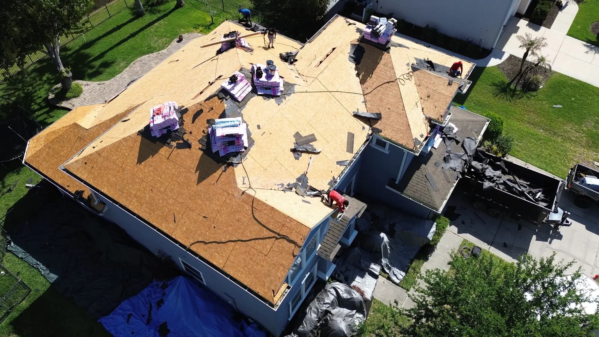 Dump trailer in a driveway filling with torn-off shingles beside a home being re-roofed